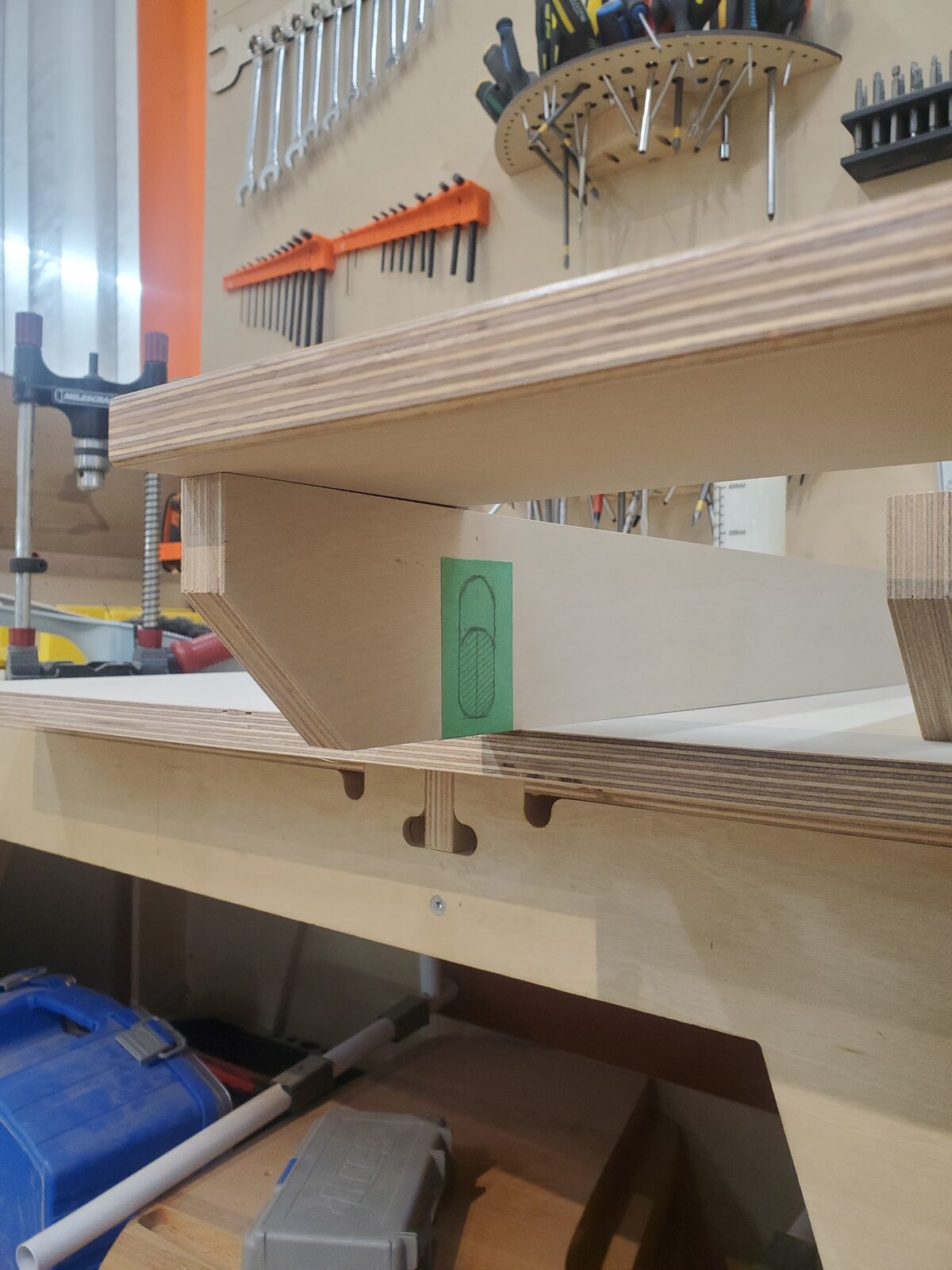 A scrap-plywood shelf mockup marked out in painter's tape, sitting on the workbench
